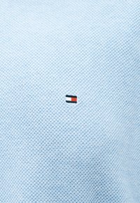 Υφασμα με γαλάζια υφή και ένα μικρό ορθογώνιο ετικέτα λογότυπου σε ναυτικό μπλε, λευκό και κόκκινο, τοποθετημένη στο κέντρο της επιφάνειας.