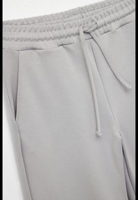 Lysgrå sweatpants lavet af blødt materiale, med en elastisk talje og snor, sidelommer og en lige benlængde.