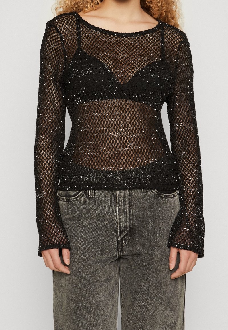 Haut à manches longues en mesh noir avec un design ajusté, présentant un motif en diamant et des poignets légèrement évasés. Superposé à un bralette noir.