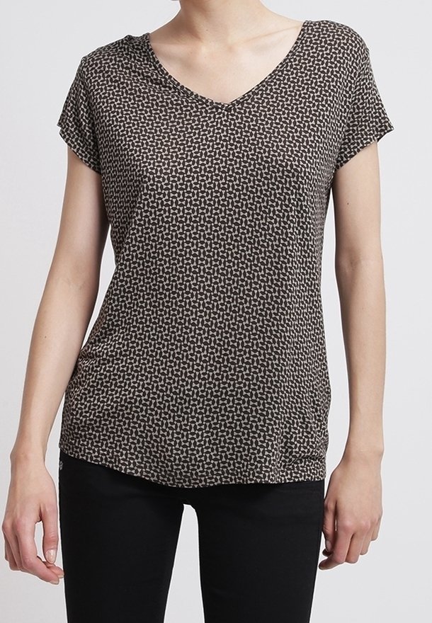 Personne portant un chemisier à manches courtes, col en V, à motif noir et blanc avec un pantalon noir, visible du cou aux hanches.