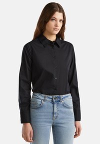 Camicia nera con colletto, realizzata in un tessuto liscio. Indossata con jeans a vita alta blu chiaro con tasche frontali.