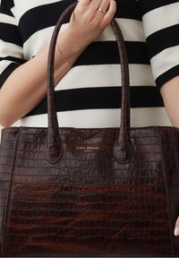 Bruine leren schoudertas met een krokodillenstructuur, uitgevoerd in een gestructureerd ontwerp, met dubbele handvatten en een goudkleurig reliëflogo aan de voorkant.