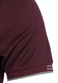 Bordeaux sportshirt van geweven stof, met een grijze zoom en multicolore strepen bij de mouwomslag voor extra detail.