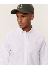 Camicia bianca con bottoni e ricamo arancione "II" sul petto sinistro. Cappellino verde oliva con un grande numero ricamato "11" e accentuazione della bandiera francese.