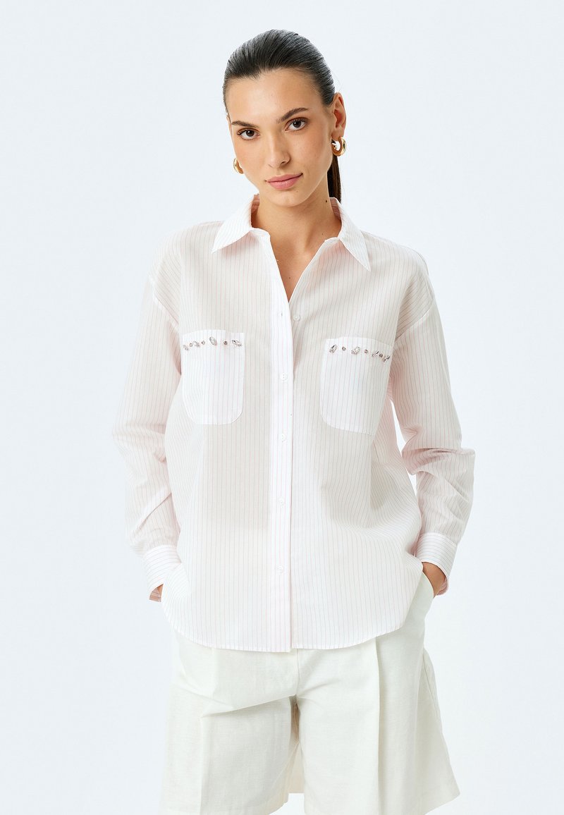 Camisa de botones a rayas de color rosa claro con dos bolsillos frontales; adornada con pequeñas piedras decorativas; mangas largas, corte relajado.