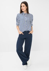 Blue and white striped button-up shirt with short sleeves paired with navy wide-leg pants, finished with white sneakers.
