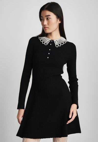 Black ribbed knit dress featuring a white decorative collar, button front, and long sleeves, with a flared skirt silhouette.