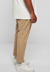 Beige chinos ar taisnu kāju piegriezumu, izgatavoti no kokvilnas, ar sānu kabatām. Valkāti ar baltām tenisēm un pelēkām zeķēm.