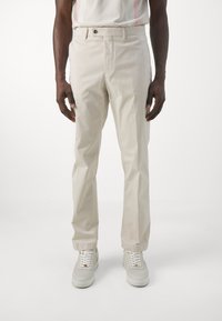 Beige bomullsbyxor med rak skärning, knappstängning fram, sidofickor och en jämn ytstruktur, i kombination med ljusgrå sneakers.