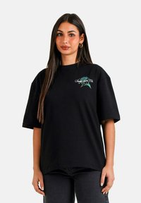 Camiseta negra de gran tamaño con mangas cortas que presenta un diseño gráfico en verde y blanco en la parte delantera. Material de algodón suave.
