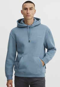 Felpa con cappuccio blu chiaro realizzata in morbido tessuto. Presenta una tasca a marsupio frontale, cappuccio con cordini e un piccolo logo sul petto.