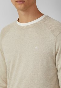 Beiger gestrickter Pullover mit geripptem Kragen und Schulterakzenten. Verfügt über ein kleines gesticktes Logo auf der linken Brust. Weiche Textur.