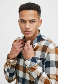 Camicia a quadri nei toni marrone, bianco e blu navy, con colletto classico e polsini regolabili, realizzata in un tessuto testurizzato.