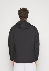 Zwarte, lichte jas met capuchon, voorzien van lange mouwen, een gestructureerd oppervlak en een ontspannen pasvorm. Geen zichtbare hardware of accenten.