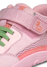 Zapatilla deportiva rosa que combina materiales de ante y malla, con cordones verdes, una tira de velcro y un sutil logo de vaca en la tira.