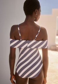 Maillot de bain une pièce présentant des rayures diagonales bleu marine et blanches, un design décolleté, des bretelles réglables et une finition textile lisse.