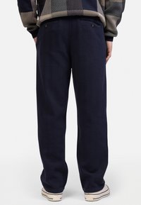 Navy blue, wide-leg trousers made from a textured fabric, featuring two back pockets with button closures and a clean, minimalist design.