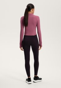 Langærmet, cropped top i mauve stof med en glat tekstur. Kombinationen med sorte, tætsiddende leggings og sorte træningssko.
