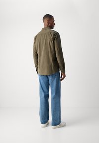 Olivengrønn kordfløyelskjorte med bakstykke, kombinert med lyseblå vidde jeans og hvite joggesko med beige detaljer.