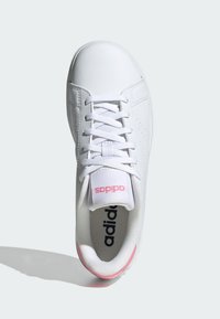 Zapatilla deportiva blanca con una parte superior sintética suave, puntera redonda, seis ojetes y un acento rosa en el talón. Presenta un suave forro textil.