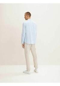 Camisa de manga larga azul claro con cuello, combinada con pantalones beige. El conjunto se completa con sneakers blancos. Diseño texturizado y informal.