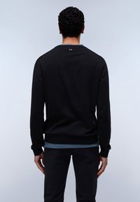 Sudadera negra con puños y dobladillo acanalados, que presenta una capa interior azul visible en la parte inferior. Pequeño detalle de logotipo rojo y blanco en el cuello.