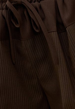 Gros plan sur un pantalon marron foncé à fines rayures avec une ceinture en tissu et un cordon de serrage assorti.