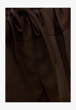 Gros plan sur un pantalon marron foncé à fines rayures avec une ceinture en tissu et un cordon de serrage assorti.