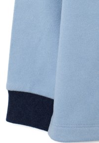 Tejido de sudadera azul claro con un acabado suave y texturizado. Presenta un puño acanalado negro marino con detalles de costura limpios.