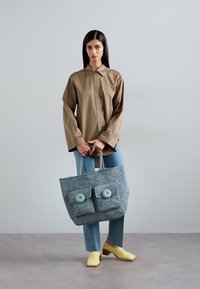 Grey fabric tote bag with two large front pockets, each featuring a circular button. The bag has sturdy handles and a textured surface.