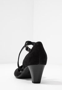 Zwarte suede hakschrijf met een ronde neus, verstelbare enkelband en een slanke aflopende hak. Gevelde afwerking met minimale accenten.