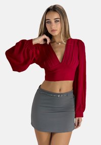 Rode cropped top met diepe V-hals en pofmouwen; gecombineerd met een strakke grijze mini-jurk met een bordeaux geklede taille. Gladde textuur.