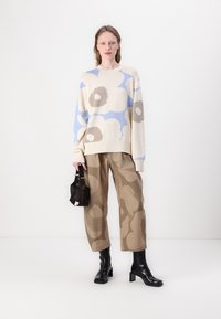 Adīta svītra kremkrāsā ar zilām un brūnām ziedu motīviem; apvienota ar taupe krāsas rakstainiem biksēm un melniem potīšu zābakiem; tur mazu melnu somu.