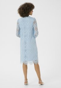 Světle modré krajkové šaty s dlouhými rukávy a vroubkovaným lemem, které mají složité květinové vzory a obtaženou siluetu.