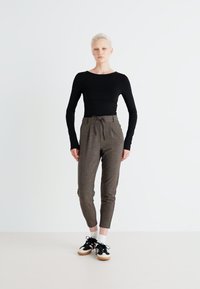 Maglietta nera a maniche lunghe abbinata a pantaloni marroni texturizzati, con vita regolabile, slim fit e scarpe da ginnastica nere casual con dettagli bianchi.