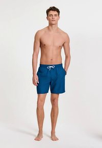 Blauwe zwembroek gemaakt van lichtgewicht stof, voorzien van een tunnelkoord in de taille en zijzakken, met een gladde textuur en een eenvoudig ontwerp.