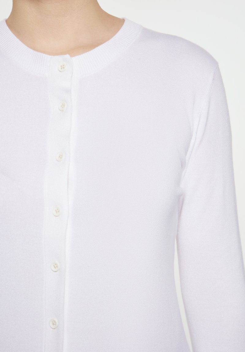 Witte cardigan van zacht breiwerk, met een ronde halslijn en een knoopsluiting in het midden met kleine, bijpassende knopen.