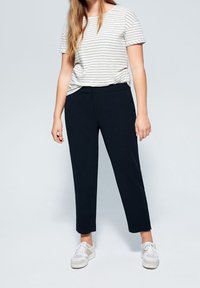 Beżowa, krótka bluzka w paski o luźnym kroju; połączona z dopasowanymi, skróconymi granatowymi spodniami i białymi trampkami. Gładka tkanina, prosty design.