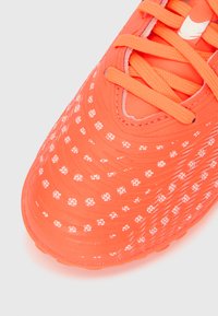 Jasnopomarańczowy but piłkarski o fakturowanym wzorze, z białymi kropkowanymi wzorami i dopasowanymi sznurowadłami. Widok z bliska podkreśla szczegóły materiału.