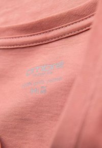 T-shirt color pesco in cotone con scollatura rotonda, con etichetta di cura in azzurro che riporta il testo "100% cotone puro" e informazioni sulla taglia.