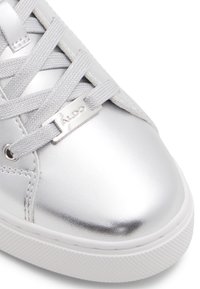 Silver metallic sneaker with smooth texture, featuring gray laces and a branded silver hardware accent. Rounded toe and rubber sole.