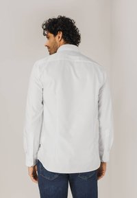 Witte blouse met lange mouwen en een kraag, casual manchet, en een gebogen zoom. Gepaard met donkerblauwe spijkerbroek. Glad textuur.