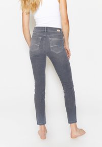 Graue Denim-Jeans mit schlankem Schnitt, standardmäßigen Gesäßtaschen und dezenten Steppdetails. Sie haben eine mittlere Leibhöhe und einen knöchellangen Schnitt.