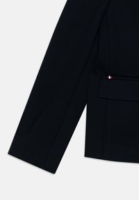 Blazer blu navy con un design strutturato, vestibilità su misura e un piccolo accento tricolore vicino alla tasca, realizzato in un tessuto liscio e testurizzato.