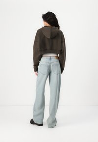 Cropped brown hoodie with a hood, paired with light blue wide-leg jeans. Black footwear visible. Simple design with a relaxed fit.