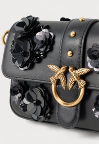Clutch de couro preto com apliques florais pretos, tachas douradas e um fecho dourado com duas aves voltadas uma para a outra.