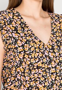 Blouse fleurie avec un fond noir orné de fleurs roses, orange et vertes, col en V et manches courtes volantées en tissu léger.