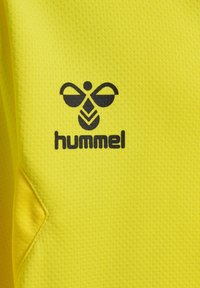 Gul atletisk skjorte med struktureret stof, med et sort bi-logo og "hummel" tekst trykt på fronten.