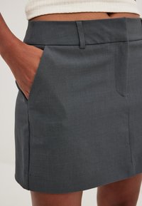 Harmaa hame, joka on valmistettu sileästä kankaasta, jossa on tasainen vyötärö, sivutaskut ja vähäiset ompeluyksityiskohdat helmassa.