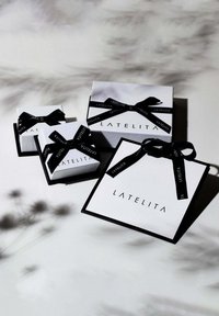 Three gift boxes of varying sizes in white with black accents. Each features a black ribbon tied into bows and the brand name "LATELITA" displayed prominently.